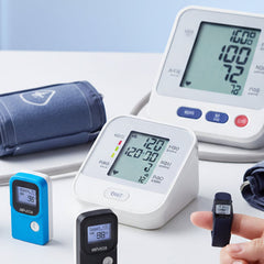 Blood pressure monitor with digital display and cuffs on a light surface.