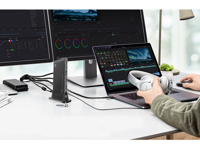 Person working on a laptop with multiple monitors displaying video editing software.