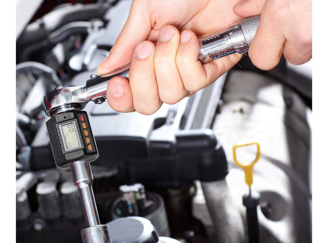 Close-up of a person using a digital torque wrench on a car engine.