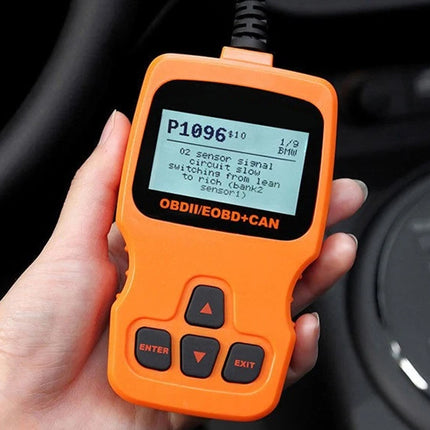An orange handheld OBDII scanner device with a black screen and buttons, held in a person's hand in front of a car dashboard.