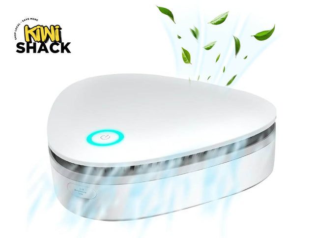 White triangular portable air purifier / mini ozone generator with a glowing cyan power button, side control button, blue mist/airflow effects and floating green leaves, branded with the Kiwi Shack logo watermark.