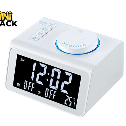 A modern white digital alarm clock with a large LED screen displaying the time, alarm status, and temperature, featuring top function buttons and a large circular snooze dial, with a "Kiwi Shack" logo in the top left corner.