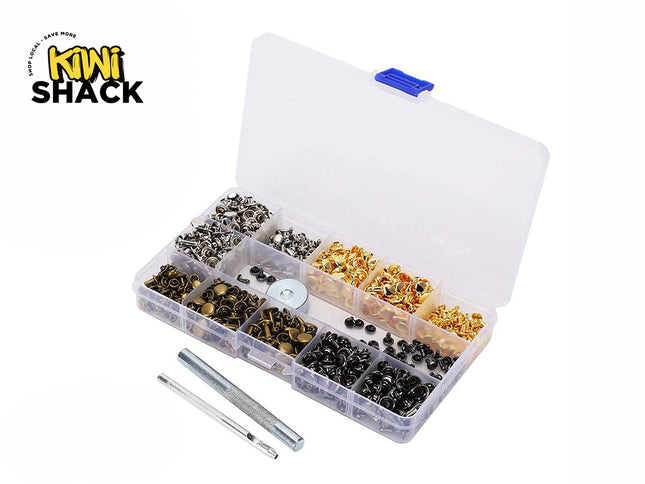 A clear plastic organizer box filled with assorted metal eyelets and rivets in black, silver, and gold finishes, shown open on a white background. Two small metal tools are placed in front.