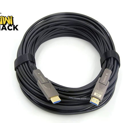A coiled black HDMI cable with gold-plated connectors and blue tip accents, secured with a black elastic band, shown on a white background with a Kiwi Shack logo in the top-left corner.
