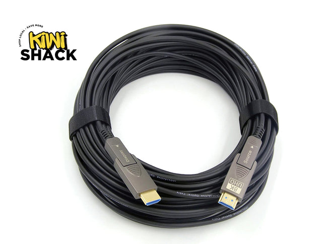 A coiled black HDMI cable with gold-plated connectors and blue tip accents, secured with a black elastic band, shown on a white background with a Kiwi Shack logo in the top-left corner.