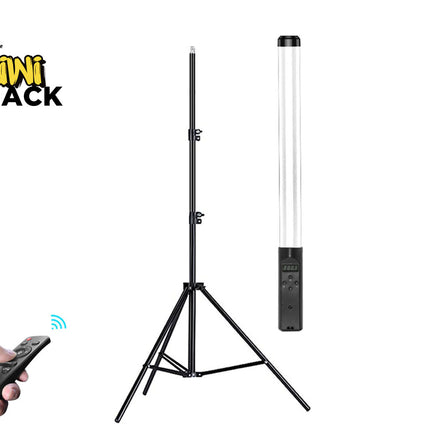 A black tripod light stand with a tall cylindrical lamp attached, shown on a white background. A hand holding a black remote control appears in the lower left, and the Kiwi Shack logo is in the upper left.
