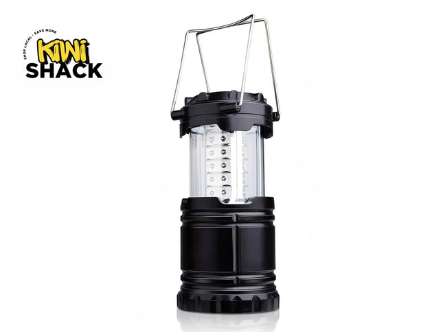 A black collapsible LED camping lantern featuring a clear plastic light column with internal LED strips and dual metal wire handle loops against a white background, featuring the "Kiwi Shack" logo in the upper left corner.