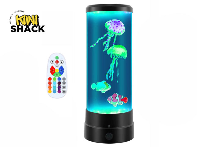 A cylindrical LED mood lamp filled with blue water containing floating artificial jellyfish and clownfish, accompanied by a white color-changing remote control on the left, set against a plain background with the "Kiwi Shack" logo in the top left corner.