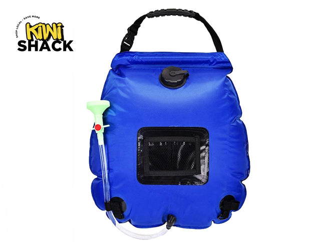 A blue portable camping shower bag featuring a top carrying handle, a fill cap, an attached clear hose with a showerhead and flow valve, a mesh front pocket, and a roll-top closure against a white background, featuring the "Kiwi Shack" logo in the upper left corner.