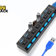 A black multi-port USB hub with individual power switches and blue LED indicators, with two USB flash drives plugged into it and a blue USB cable extending outward, set against a white background with the "Kiwi Shack" logo in the top left corner.