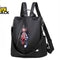 A black nylon convertible backpack purse featuring a diagonal front zipper with two cat-shaped keychains attached.