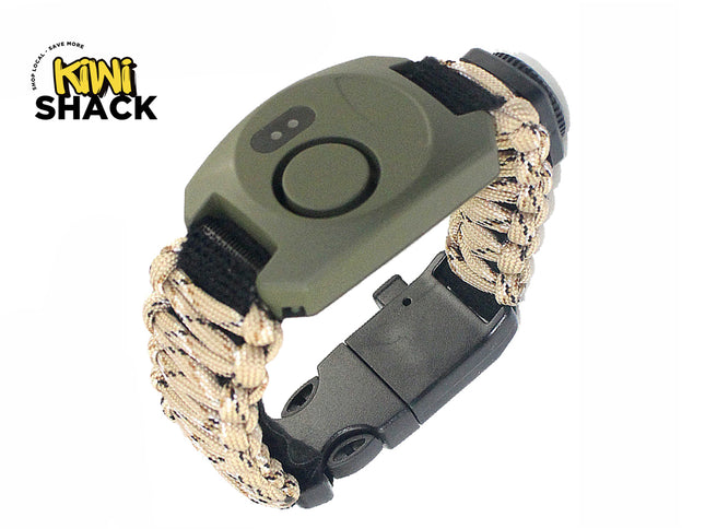 An olive green and tan paracord survival bracelet featuring an integrated digital compass, whistle, and a black plastic side-release buckle, with a "Kiwi Shack" logo in the top left corner.