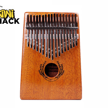 A wooden 17-key kalimba thumb piano with engraved note letters on the metal tines, a sound hole encircled by a decorative floral design, and a trapezoidal body against a white background, featuring the "Kiwi Shack" logo in the upper left corner.