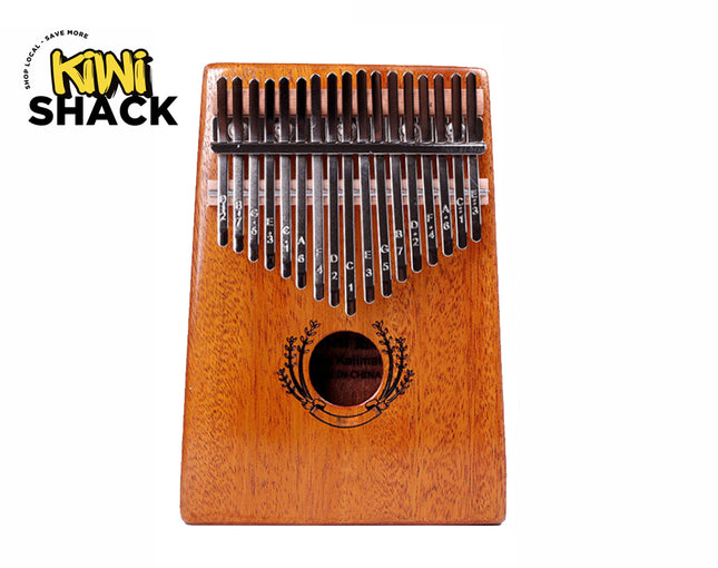 A wooden 17-key kalimba thumb piano with engraved note letters on the metal tines, a sound hole encircled by a decorative floral design, and a trapezoidal body against a white background, featuring the "Kiwi Shack" logo in the upper left corner.