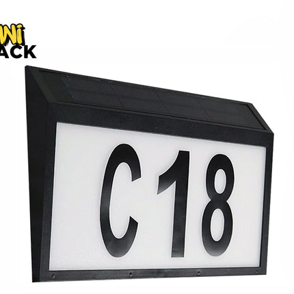 A black rectangular solar-powered address sign featuring illuminated white display panels with large bold black characters "C18" and an integrated solar panel on the slanted top surface against a white background, featuring the "Kiwi Shack" logo in the upper left corner.