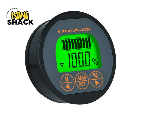 A round black battery indicator display unit with a green backlit LCD screen showing 100% battery level and orange buttons below, on a white background with a Kiwi Shack logo in the top-left corner.