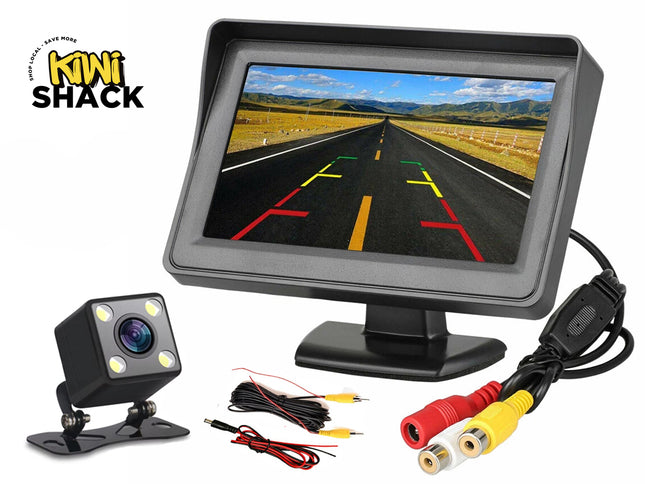 A car backup camera kit with a dashboard display monitor showing parking grid lines, a square LED backup camera, and connection cables, featuring the "Kiwi Shack" logo in the top-left corner.