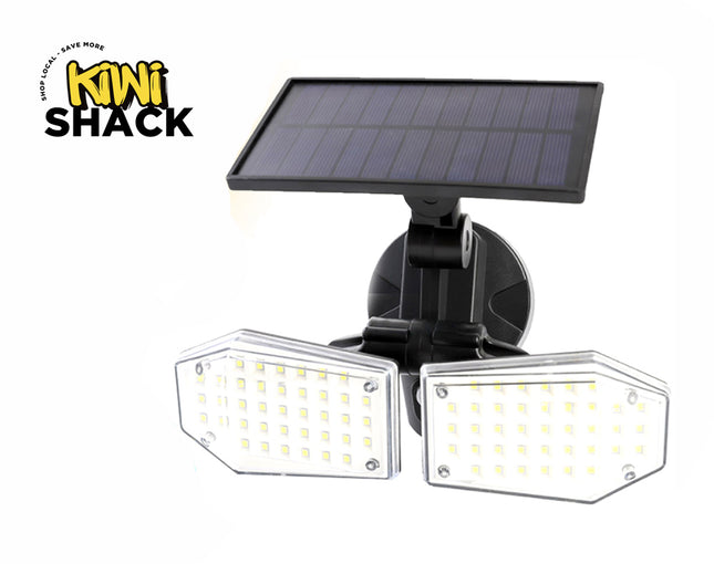 A dual-head solar-powered LED floodlight with individual multi-LED diode panels behind clear protective covers, mounted on an adjustable black bracket beneath an attached photovoltaic solar panel against a white background, featuring the "Kiwi Shack" logo in the upper left corner.