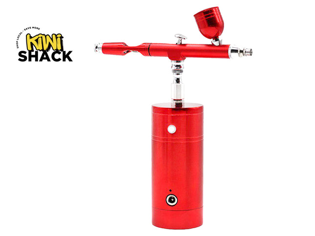A red airbrush air compressor with a matching red cup and silver metal components, shown on a white background with the Kiwi Shack logo in the top-left corner.