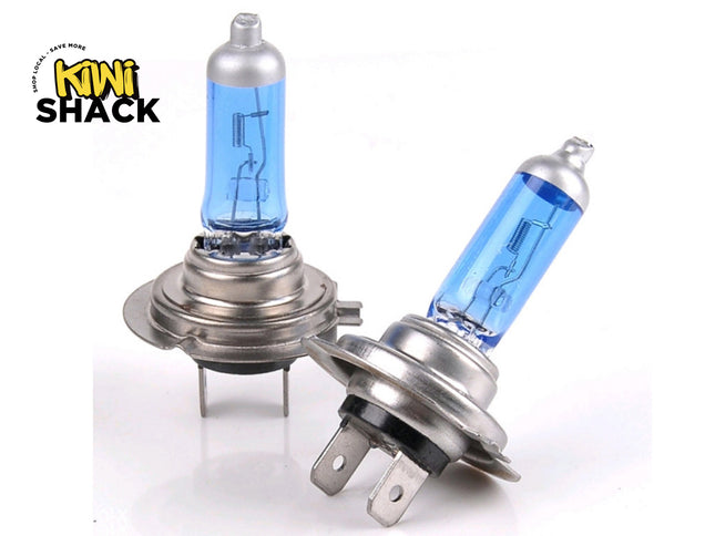 Pair of blue-tinted automotive halogen headlight bulbs with metal mounting flanges, internal filament loops, electrical spade connectors at the base, and Kiwi Shack logo in top left.