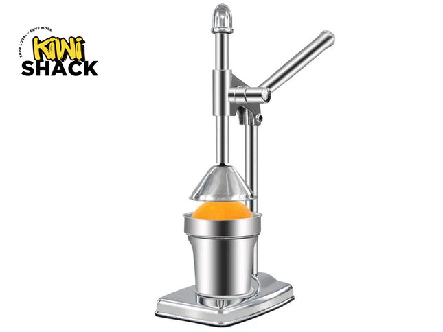 A stainless steel manual mini citrus juicer with a lever arm and cone press, shown with an orange inside the collection cup on a white background. The 'Kini Shack' brand logo is visible in the top-left corner.