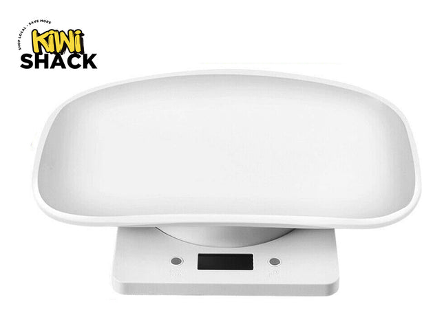 A white digital baby scale featuring a wide, curved weighing tray on top and a rectangular base with a digital screen and control buttons in the front, with a "Kiwi Shack" logo in the top left corner.