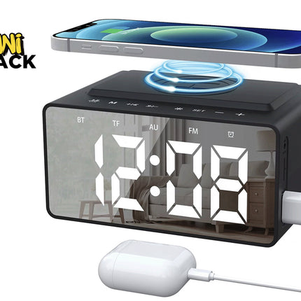 A black digital alarm clock radio with a mirrored display showing white time numbers, a top wireless charging pad holding a smartphone, a side-mounted USB charging cable, and a wired white charging case against a white background, featuring the "Kiwi Shack" logo in the upper left corner.