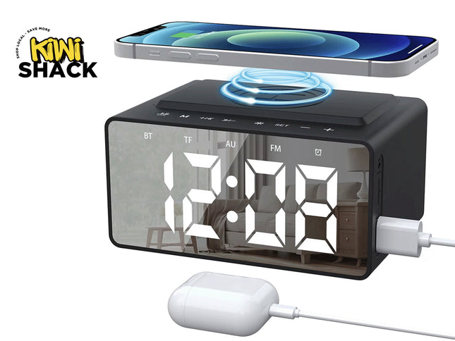 A black digital alarm clock radio with a mirrored display showing white time numbers, a top wireless charging pad holding a smartphone, a side-mounted USB charging cable, and a wired white charging case against a white background, featuring the "Kiwi Shack" logo in the upper left corner.
