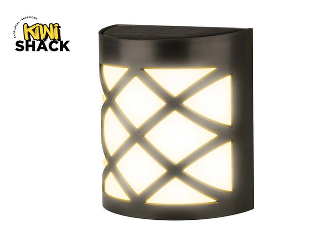 A black outdoor wall light fixture by Mini Shack, featuring a cylindrical body with a crisscross cutout pattern that illuminates a warm white light. The Mini Shack logo is visible in the top-left corner.