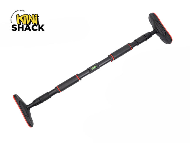 An adjustable black and red doorway pull-up bar angled across a white background, featuring extended non-slip textured rubber base pads at both ends and a built-in bubble level near the center, with a "Kiwi Shack" logo in the top left corner.