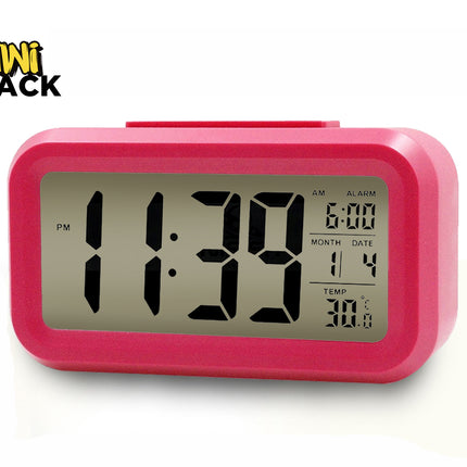 A vibrant pink digital desktop alarm clock featuring a large LCD screen with bold black numbers indicating 11:39 PM, an alarm time set to 6:00, calendar month and date, and a temperature display in Celsius against a white background, featuring the "Kiwi Shack" logo in the upper left corner.