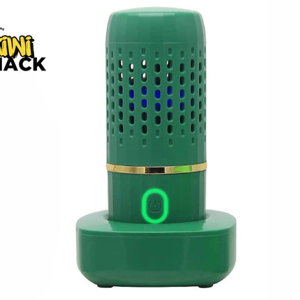 A green electronic fruit and vegetable cleaner on a matching charging base, featuring a glowing green power button and a vented cylindrical body with blue light inside, featuring a "Kiwi Shack" logo in the top left corner.