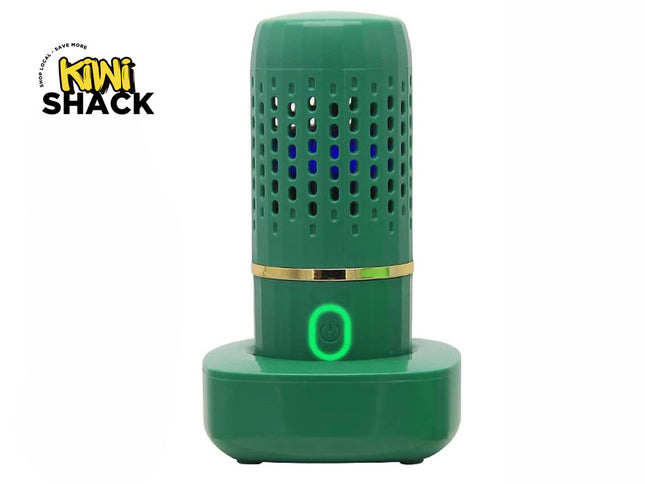 A green electronic fruit and vegetable cleaner on a matching charging base, featuring a glowing green power button and a vented cylindrical body with blue light inside, featuring a "Kiwi Shack" logo in the top left corner.