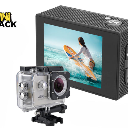 A 4K action camera shown both bare with its textured black housing and back display, and encased in a clear waterproof protective housing mounted on a base, with the screen displaying a surfer on a yellow board against a white background, featuring the "Kiwi Shack" logo in the upper left corner.