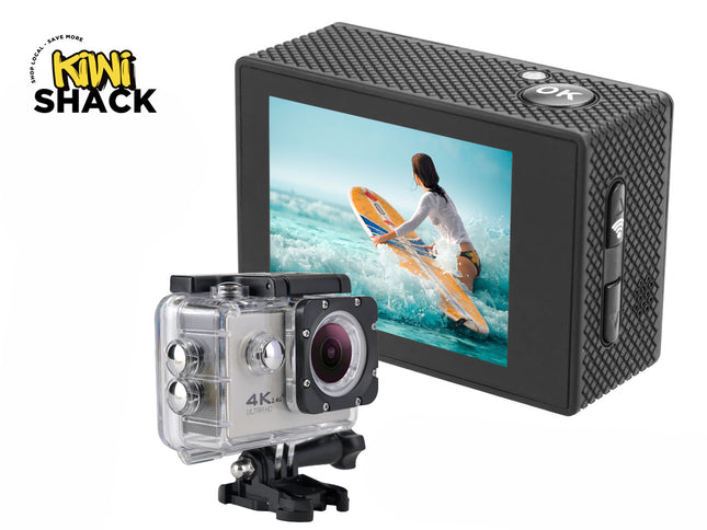 A 4K action camera shown both bare with its textured black housing and back display, and encased in a clear waterproof protective housing mounted on a base, with the screen displaying a surfer on a yellow board against a white background, featuring the "Kiwi Shack" logo in the upper left corner.
