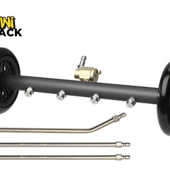 Product shot of a black undercarriage pressure washer attachment with two black wheels on either end, four stainless steel spray nozzles along the bar, a brass inlet valve with a quick-connect plug at the top center, and three extension wands placed underneath. The 'Kiwi Shack' logo appears in the top left corner.