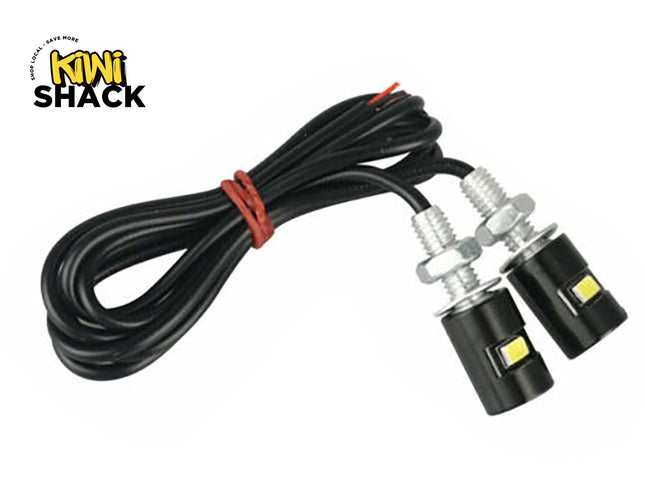 Pair of black bolt-on LED eagle eye lights with threaded mounting studs, nuts, washers, and long wired lead tied with red twist tie, featuring Kiwi Shack logo in top left.
