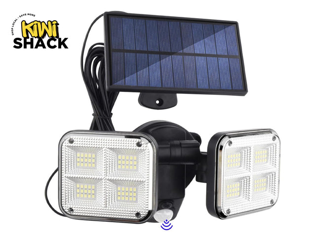 A dual-head solar-powered motion sensor LED floodlight featuring four square multi-LED diode panels on each light head, connected via a long cord to a separate photovoltaic solar panel against a white background, featuring the "Kiwi Shack" logo in the upper left corner.