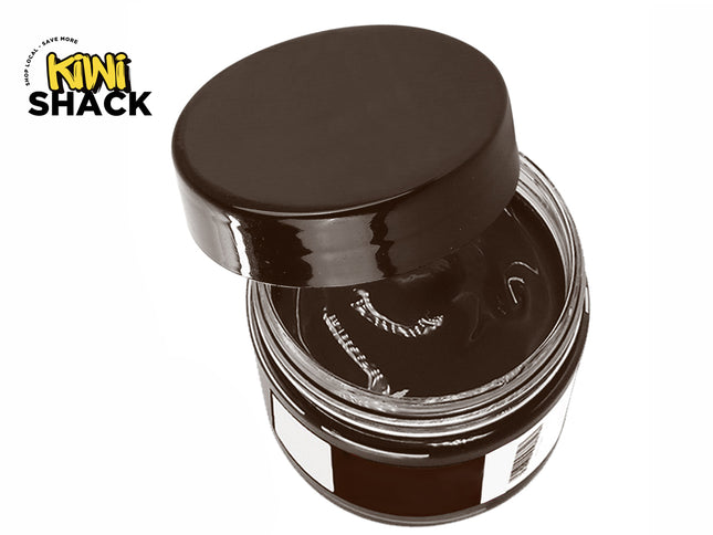 An open glass jar of dark brown shoe polish with its matching dark lid tilted off to the side, revealing a smooth waxy surface against a white background, featuring the "Kiwi Shack" logo in the upper left corner.
