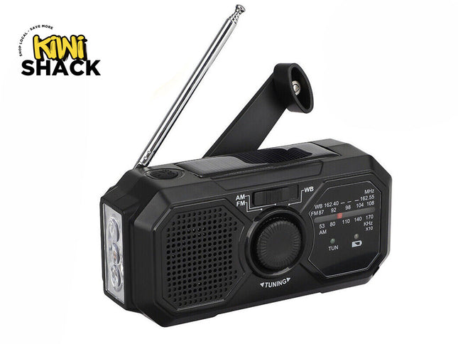 A black emergency weather radio featuring an extendable antenna, a hand crank, a built-in solar panel, a flashlight on the side, and a tuning dial, with a "Kiwi Shack" logo in the top left corner.