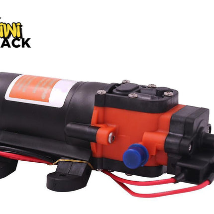 A small electric pump motor with a black cylindrical body, orange casing, black mounting feet, a blue connector cap, and red wires, shown on a white background with the Kiwi Shack logo in the top-left corner.
