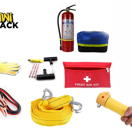 A comprehensive roadside emergency and safety kit laid out against a white background, including a red fire extinguisher, a blue reflective warning triangle case, a red "FIRST AID KIT" bag, heavy-duty jumper cables, a yellow tow strap with hooks, a tire repair set, a pair of work gloves, and a hand holding a yellow emergency escape hammer, with the "Kiwi Shack" logo in the upper left corner.