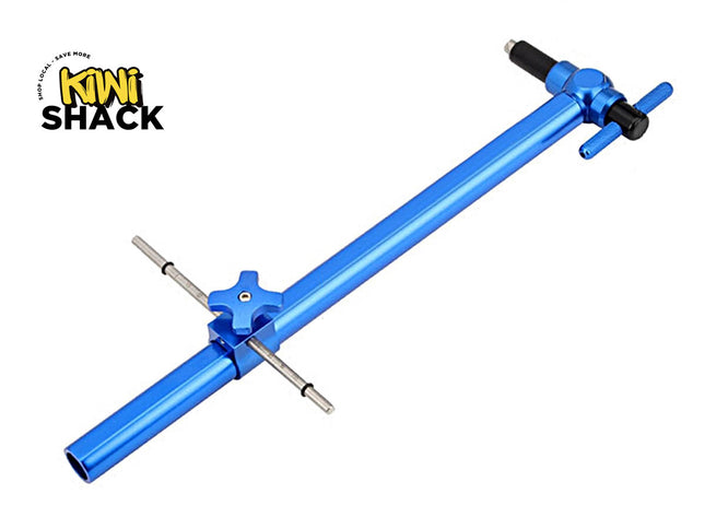 A blue anodized aluminum bicycle chainstay tensioner tool with silver metal pins and black adjustment knobs, shown on a plain white background with the Kiwi Shack logo in the top-left corner.