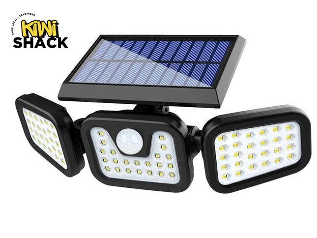 A three-light solar-powered outdoor floodlight with a central motion sensor, featuring a black housing, three adjustable LED lamp heads, and a blue solar panel on top. The Kiwi Shack logo is visible in the top left corner.