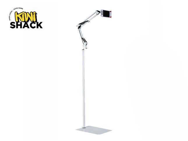 A tall white floor stand for a phone or tablet, featuring a flat rectangular base, a vertical extension pole, an articulated spring-loaded mechanical arm at the top, and a device clamp holding a phone, with the "Kiwi Shack" logo in the top left corner.