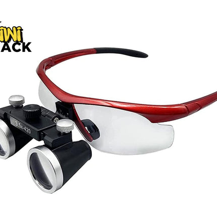 A pair of surgical magnifying glasses with a red frame, clear lenses, and a black double-ocular microscope attachment. The Kiwi Shack logo is visible in the top-left corner.