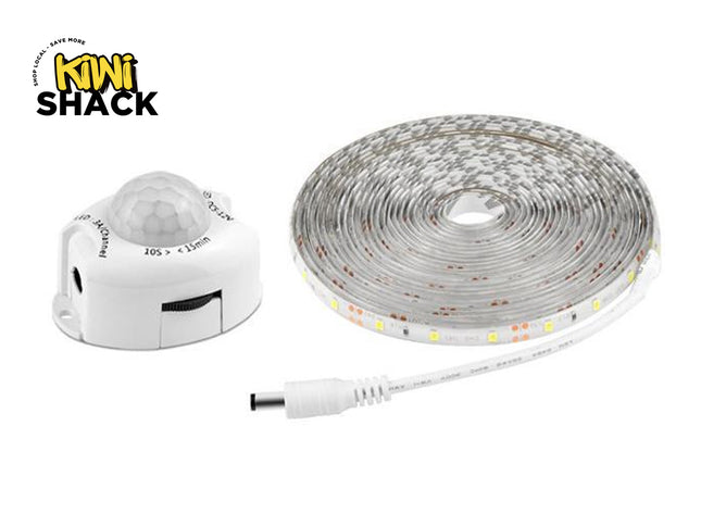 A white motion sensor unit with a hemispherical dome and a coiled roll of LED strip lighting featuring a DC power connector, set against a white background. A "Kiwi Shack" logo appears in the top-left corner.