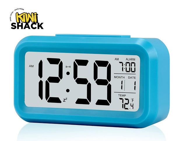 A bright blue digital desktop alarm clock featuring a large LCD screen with bold black numbers, an alarm time of 7:00, calendar month and date, temperature display in Fahrenheit, and a snooze icon against a white background, featuring the "Kiwi Shack" logo in the upper left corner.