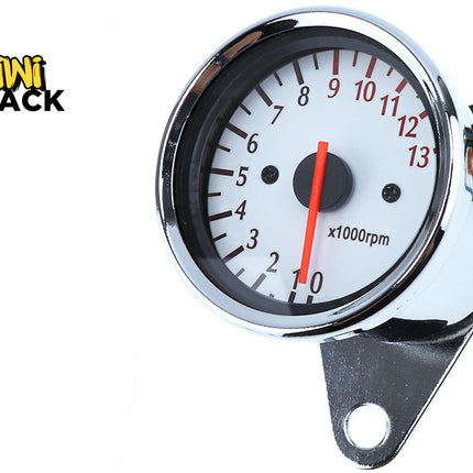 A chrome-framed motorcycle tachometer gauge with a white dial face, black numbering up to 13 (x1000 rpm), a red indicator needle, a mounting bracket at the base, and colored wires extending from the back against a white background, featuring the "Kiwi Shack" logo in the upper left corner.