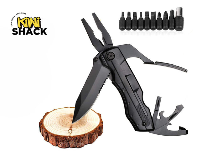 A black tactical multi-tool featuring a combination knife blade with a serrated edge resting on a wooden log slice, extended pliers, additional fold-out tools, and a set of interchangeable screwdriver bits shown in the upper right, against a white background, featuring the "Kiwi Shack" logo in the upper left corner.